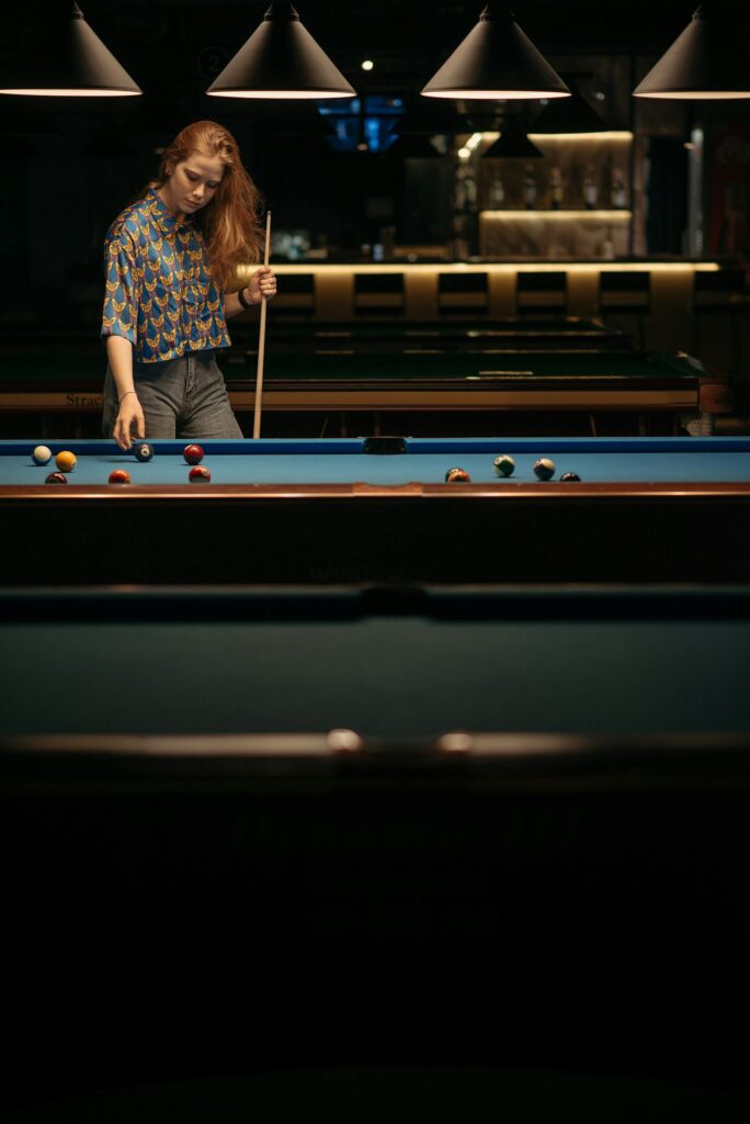 Woman standing beside a billiards table in a pool hall, used for women's billiards social content.